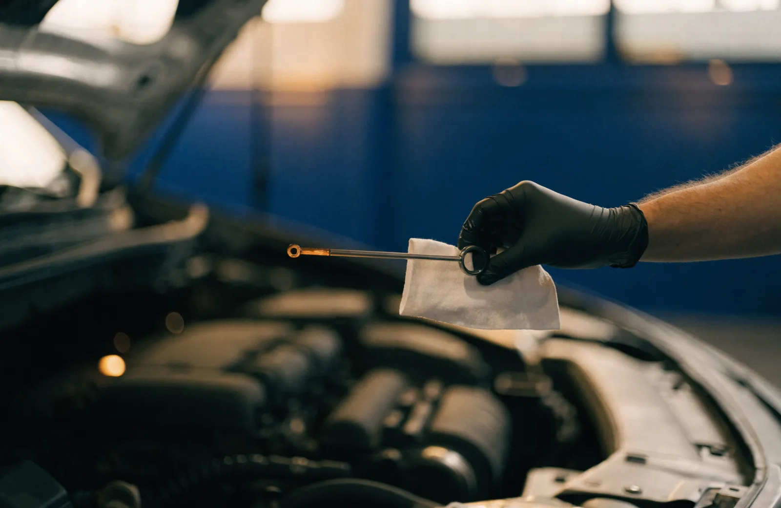 Technician checking an engine oil dipstick over a shop rag for a rising oil level