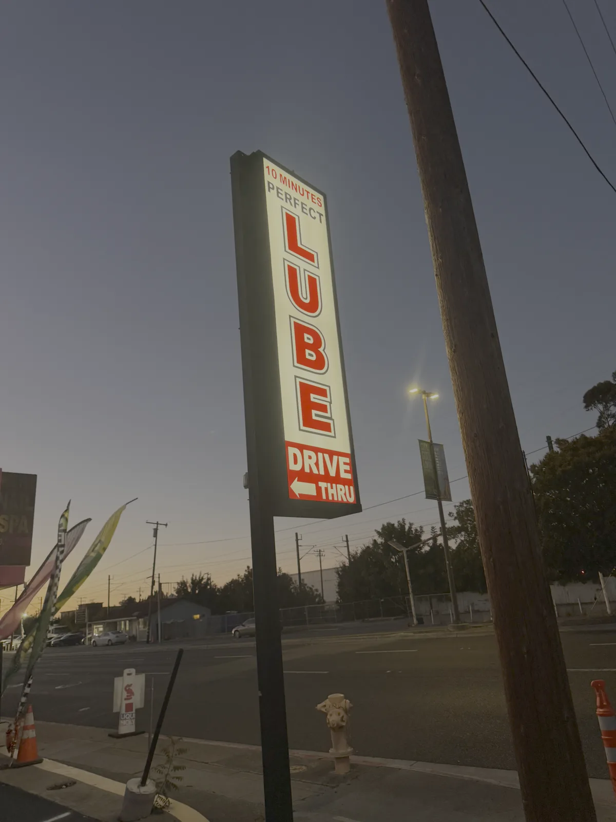 Perfect Lube's illuminated 10 Minutes Drive Thru sign lit up at dusk on El Camino Real in San Carlos