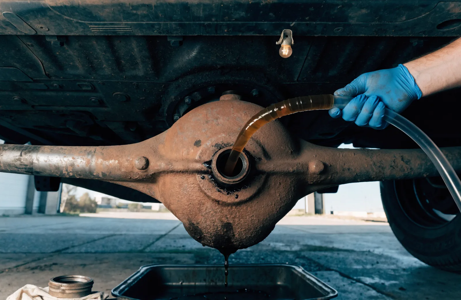 Fresh gear oil being pumped into the fill hole of a rear differential on a truck raised on a lift