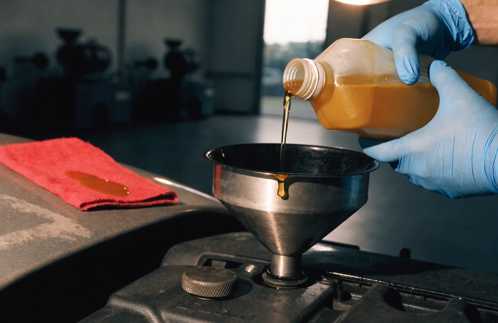 Fresh motor oil poured from a just-opened bottle through a funnel into an engine during a drive-thru oil change