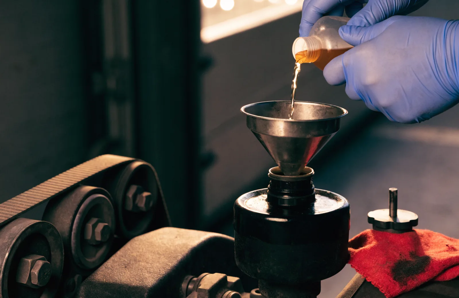 Power steering fluid being poured through a funnel into an open reservoir beside the serpentine belt